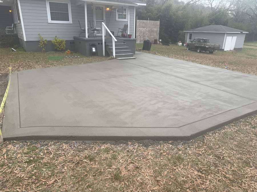 Broad finished concrete surface beside a wooden deck and fence.