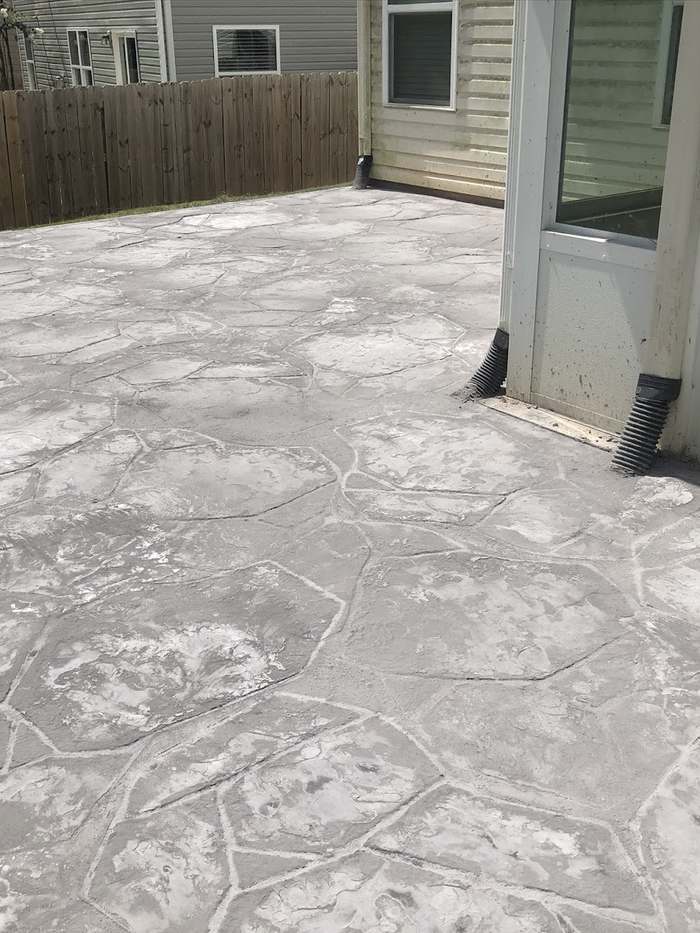 Stamped concrete patio surface beside a home and fenced yard.